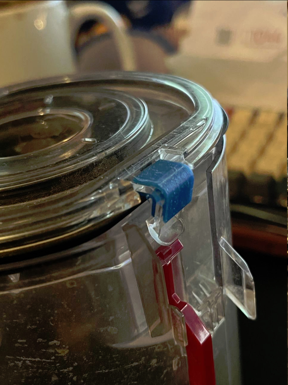 La pièce imprimée en plastique bleu et installée temporairement sur le bac de l'aspirateur afin de tester la réparation le clip.